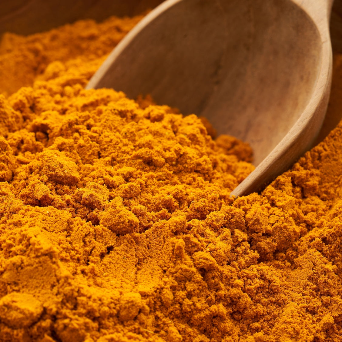 Raw curcumin ingredient being scooped by a wooden spoon.